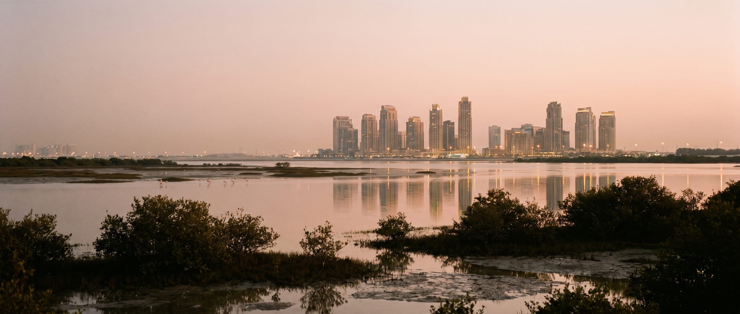 Wide dusk view of Dubai Creek Harbour towers across the creek with mangroves in the foreground