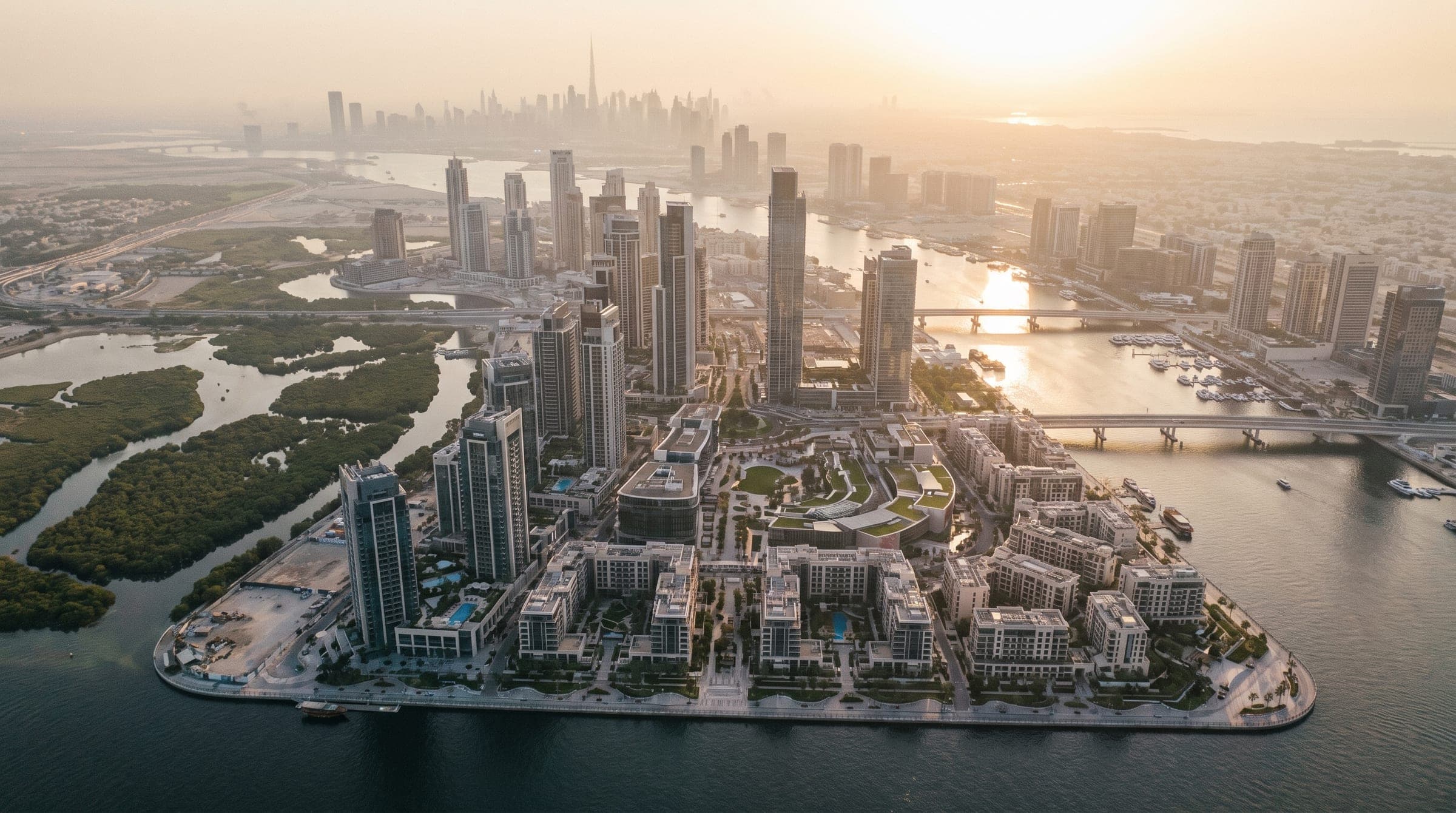 High aerial of the Dubai Creek Harbour masterplan at golden hour: island district, bridges, creek and wetlands